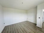 Empty, unfurnished kitchen space with light wood flooring and a white tiled wall area for future cabinets; exposed plumbing near the corner.