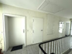 White hallway with multiple white doors along a textured beige wall; a black handrail is visible in the foreground.